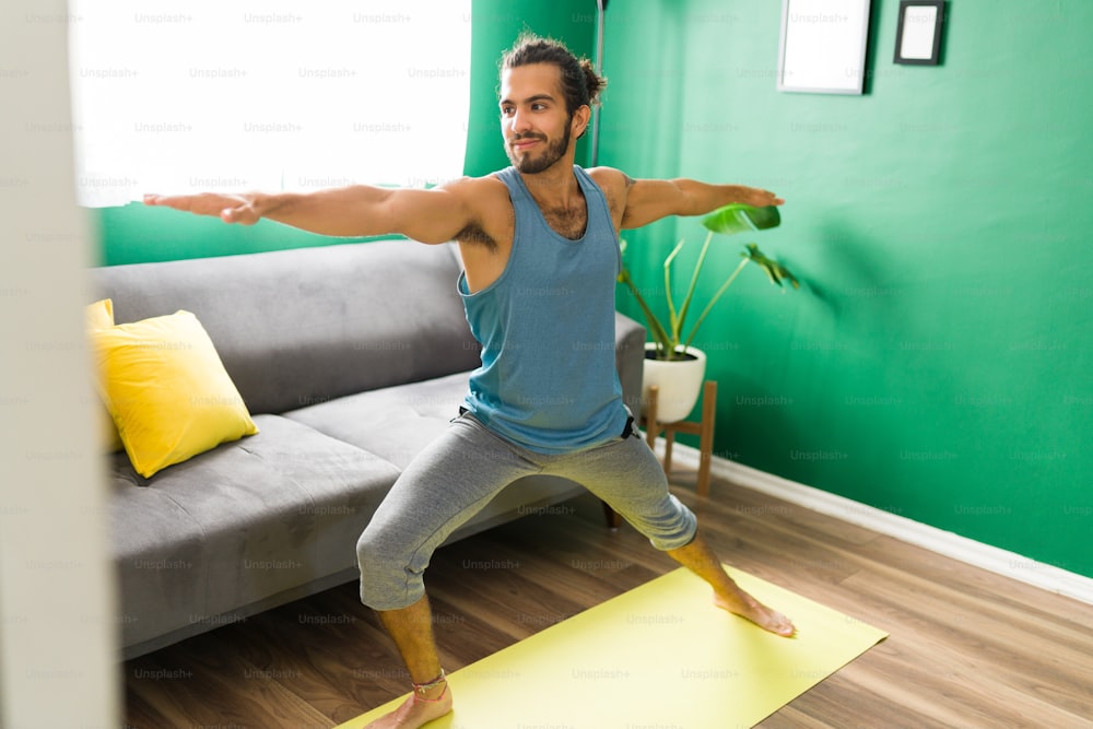 Good-looking young man practicing a warrior yoga pose in his living room. Active man working out with a yoga routine