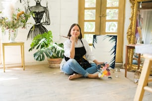 Porträt einer jungen Frau, die auf Inspiration wartet, während sie in einem Kunstatelier ein wunderschönes Gemälde malt
