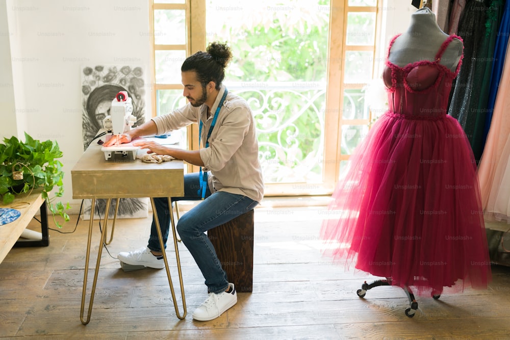 Creative young man and seamstress sewing a new elegant dress for a customer at the studio