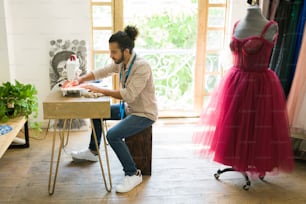 Joven creativo y costurera cosiendo un nuevo vestido elegante para un cliente en el estudio