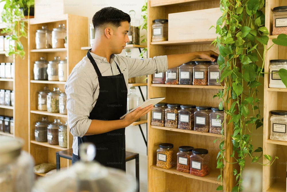 Jovem trabalhador atraente reabastecendo os recipientes com produtos orgânicos na loja a granel ecológica