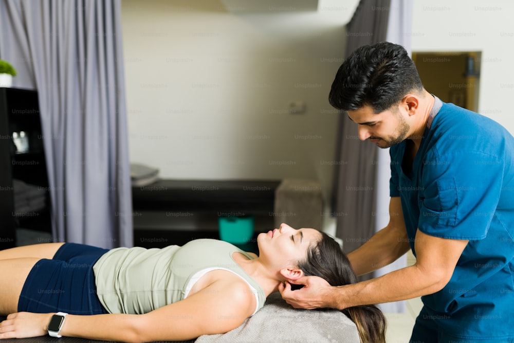 Fisioterapeuta bonito dando uma massagem no pescoço a uma paciente jovem na clínica