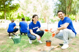 Trabalho comunitário ecológico. Amigos latinos felizes plantando juntos uma pequena árvore no parque para o seu trabalho voluntário