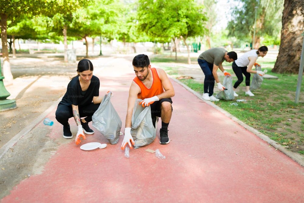 Quiero un parque limpio. Grupo de amigos responsables de unos 20 años recogiendo basura al aire libre mientras hacen ejercicio juntos