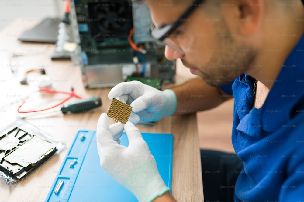 Close up of a young technician wearing protection glasses and gloves while checking the damaged microprocessor chip of a computer