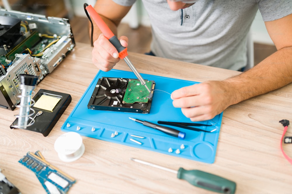 Close up of the technician's hands soldering tin to solder and repair a hard drive on a broken computer CPU