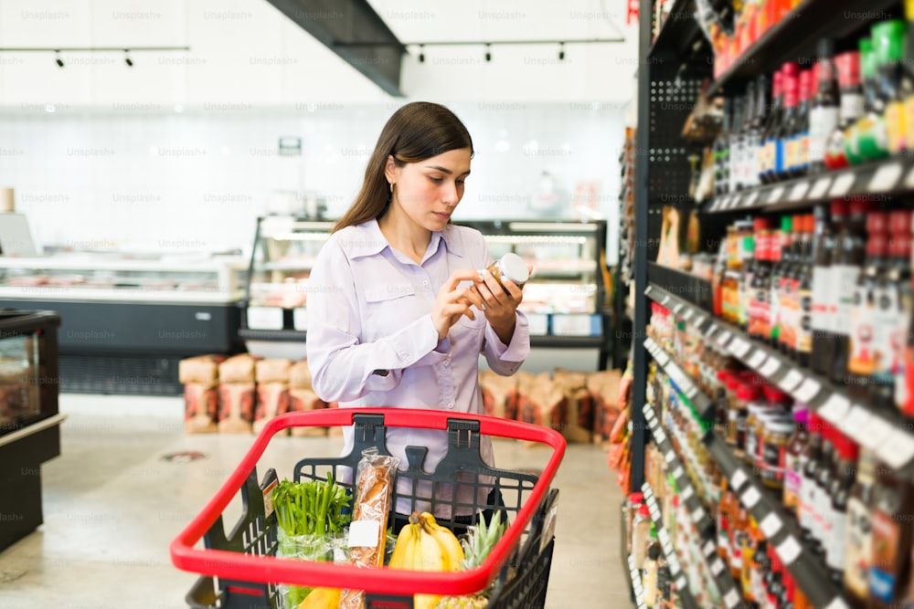Jeune femme intelligente lisant l’étiquetage du produit et vérifiant les informations nutritionnelles d’un produit alimentaire au supermarché