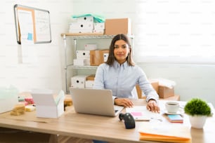 Retrato de uma jovem empreendedora hispânica sentada em sua mesa de escritório e trabalhando na confecção de pacotes para enviar aos seus clientes