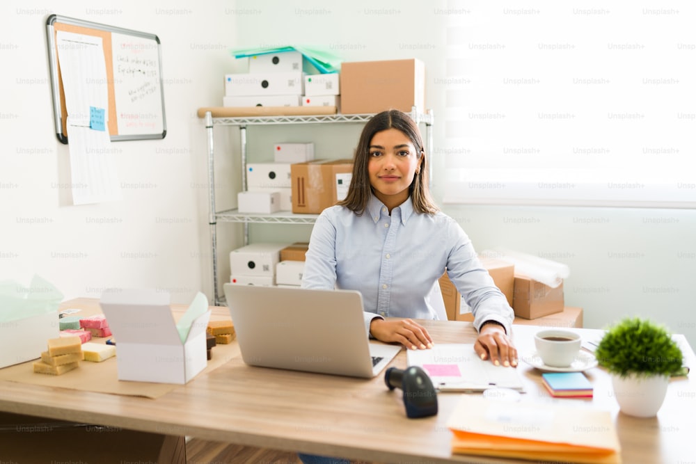 Portrait of an hispanic young entrepreneur sitting at her office desk and working on making packages to ship to their customers
