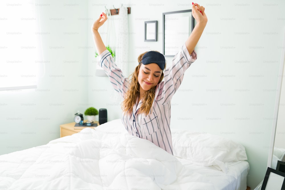 Mujer hispana emocionada estirando los brazos y sonriendo después de despertarse por la mañana. Mujer feliz en pijama sintiéndose bien en su cómoda cama