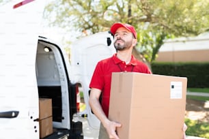 Handsome male courier delivering a big package at a home or business shipping address. Delivery man in his 30s feeling proud of his work