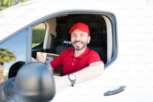 Handsome latin man wearing a red uniform and preparing to start his route to deliver packages in the city. Delivery man driving to a shipping address