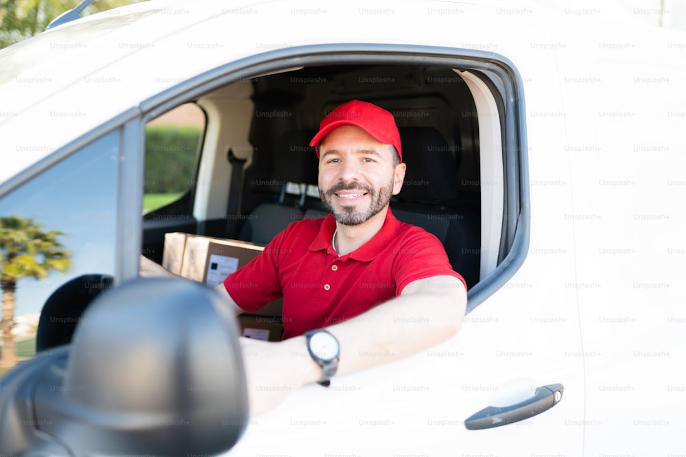 Handsome latin man wearing a red uniform and preparing to start his route to deliver packages in the city. Delivery man driving to a shipping address