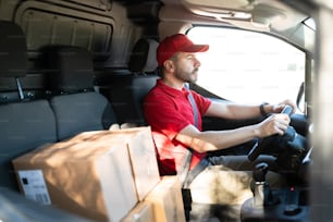 Focused delivery man driving a white van with a lot of packages and boxes. Hispanic courier en route to deliver packages at a home or business in the city