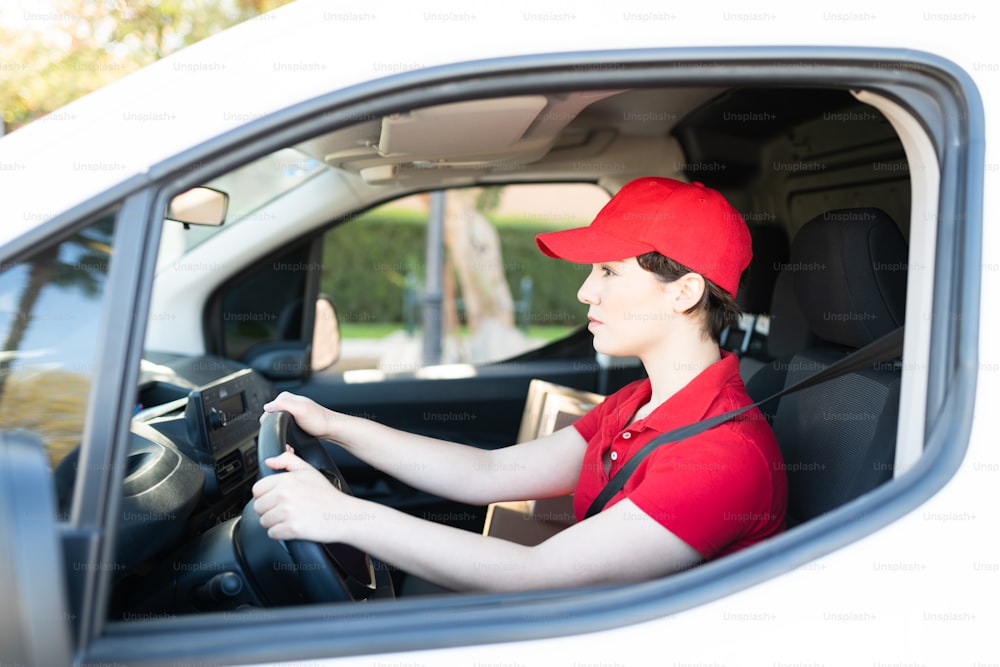 Profile of an attractive caucasian woman driving a white delivery truck. Female courier en route to deliver packages at a home or business in the city