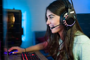 Mujer joven hablando con auriculares y un micrófono a un jugador o amigo en línea mientras juega un videojuego en su computadora de juegos