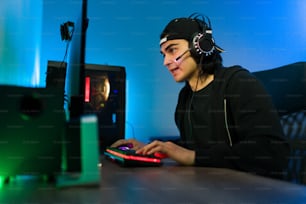 Jovem latino falando com fones de ouvido e um microfone para um jogador ou amigo on-line enquanto joga um videogame no computador