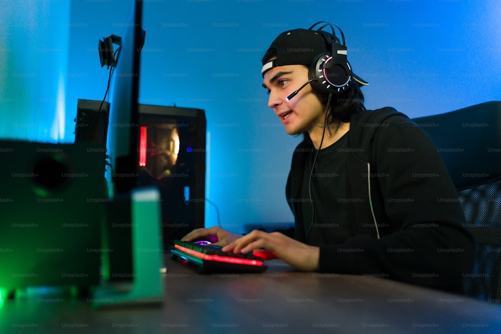 Young latin man talking with headphones and a microphone to an online player or friend while playing a video game on the computer