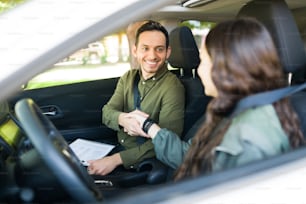 Handsome male instructor shaking hands and greeting a teen girl for her driving lessons. Latin man teaching an adolescent how to drive a car