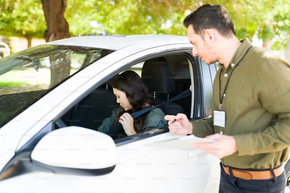 Male instructor guiding a teenage girl during her exam to get a driver's licence. Hispanic man telling an adolescent girl to put on her seatbelt