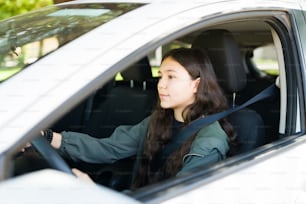 Pretty teen girl paying attention to the road while driving a car with the seatbelt on. Excited caucasian girl going out after getting her driver's license