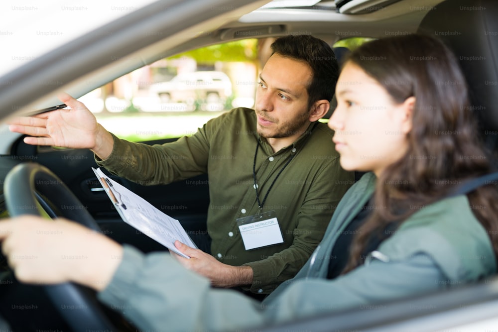 Handsome man in his 30s and beautiful teen girl sitting inside a car for a driving exam. Male instructor giving directions to an adolescent girl during her lesson