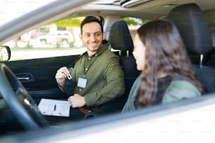 Istruttore maschio felice che sorride e insegna a una studentessa adolescente a guidare. Ragazza adolescente che si sente nervosa durante la sua prima lezione di guida
