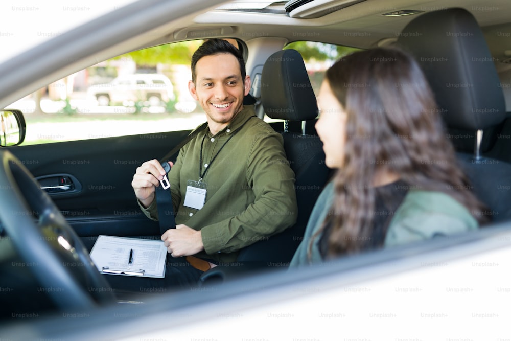 Happy male instructor smiling and teaching a teenage girl student to drive. Adolescent girl feeling nervous during her first driving lesson