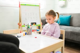 Hübsches kleines Mädchen mit schlechtem Benehmen, das während einer Kindertherapiesitzung im Büro des Psychologen etwas über Disziplin und Selbstbeherrschung lernt