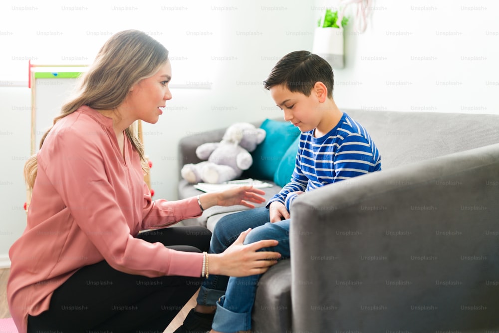 Confortando a psicóloga feminina conversando com um menino por causa de seus tristes sentimentos e emoções negativas durante uma sessão de terapia infantil