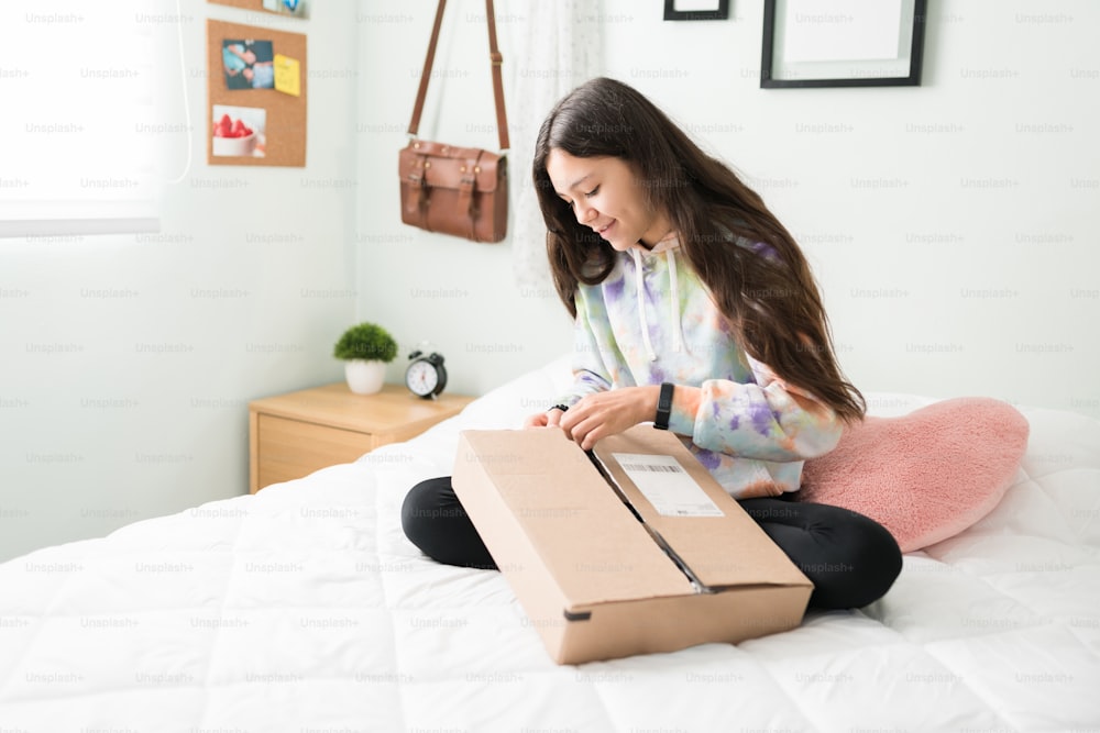Hübsches Teenager-Mädchen erhielt ein Paket mit der Post. Kaukasische Jugendliche sitzt in ihrem Schlafzimmer und öffnet eine Schachtel mit ihrem Online-Einkauf