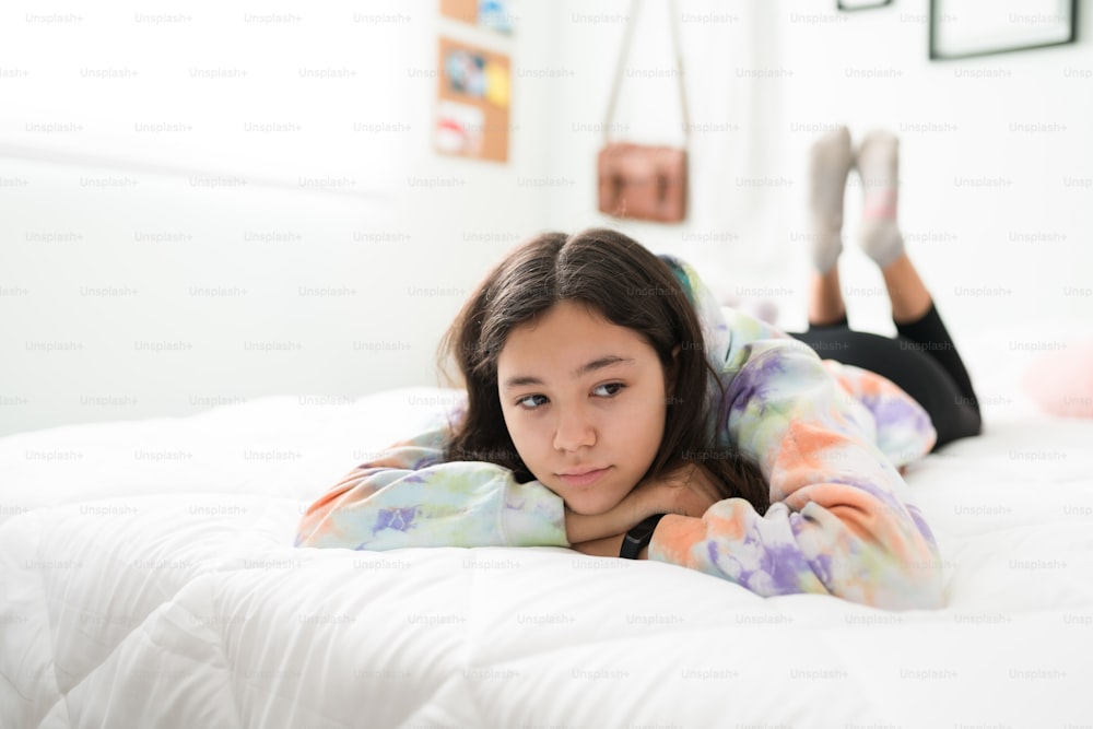 Adolescente caucasiana entediada deitada de bruços na cama e relaxando. Adolescente cansada tendo um dia de lazer em seu quarto