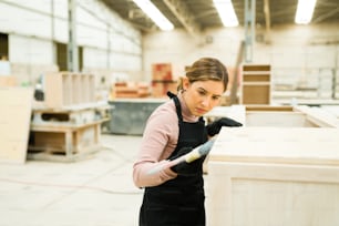 Jeune femme de race blanche portant un tablier et utilisant un pinceau pour peindre une armoire de cuisine en bois sur un atelier de menuiserie