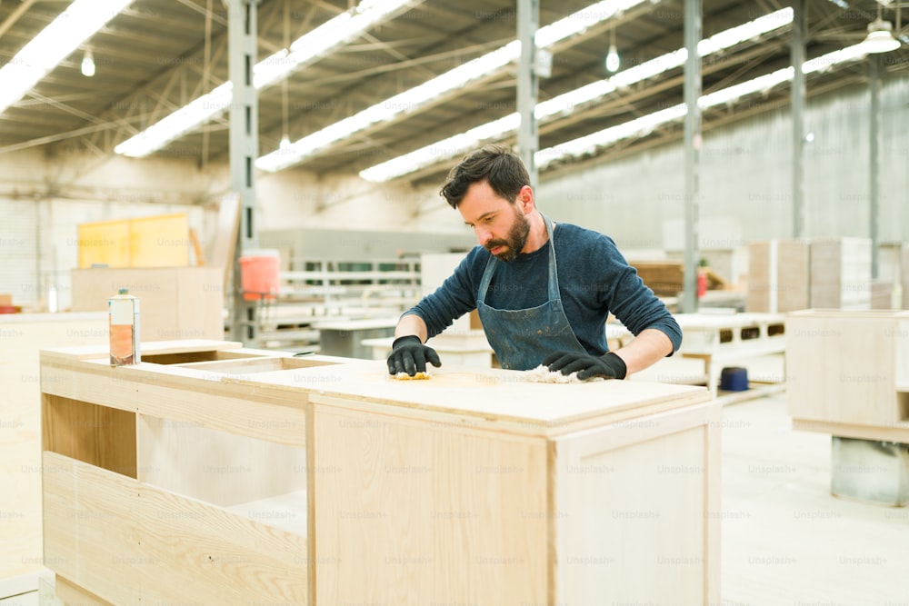 Bel homme latin travaillant à la finition d’une armoire de cuisine. Charpentier professionnel utilisant la teinture à l’huile de bois dans un meuble