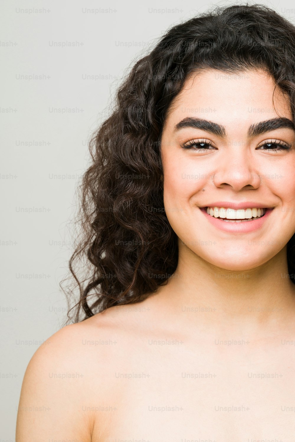 Happy latin woman in her 20s smiling. Cropped photo of a young woman and beauty model with healthy skin and nude shoulders