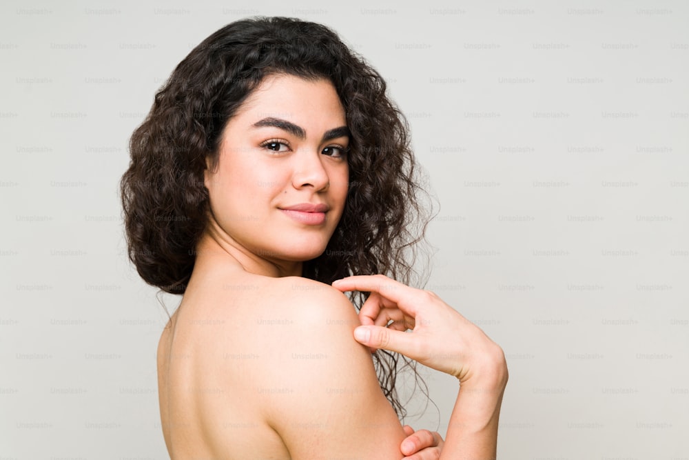 Side view of an attractive hispanic woman in her 20s smiling. Female model with natural skin and nude shoulders ready to go to the beauty spa