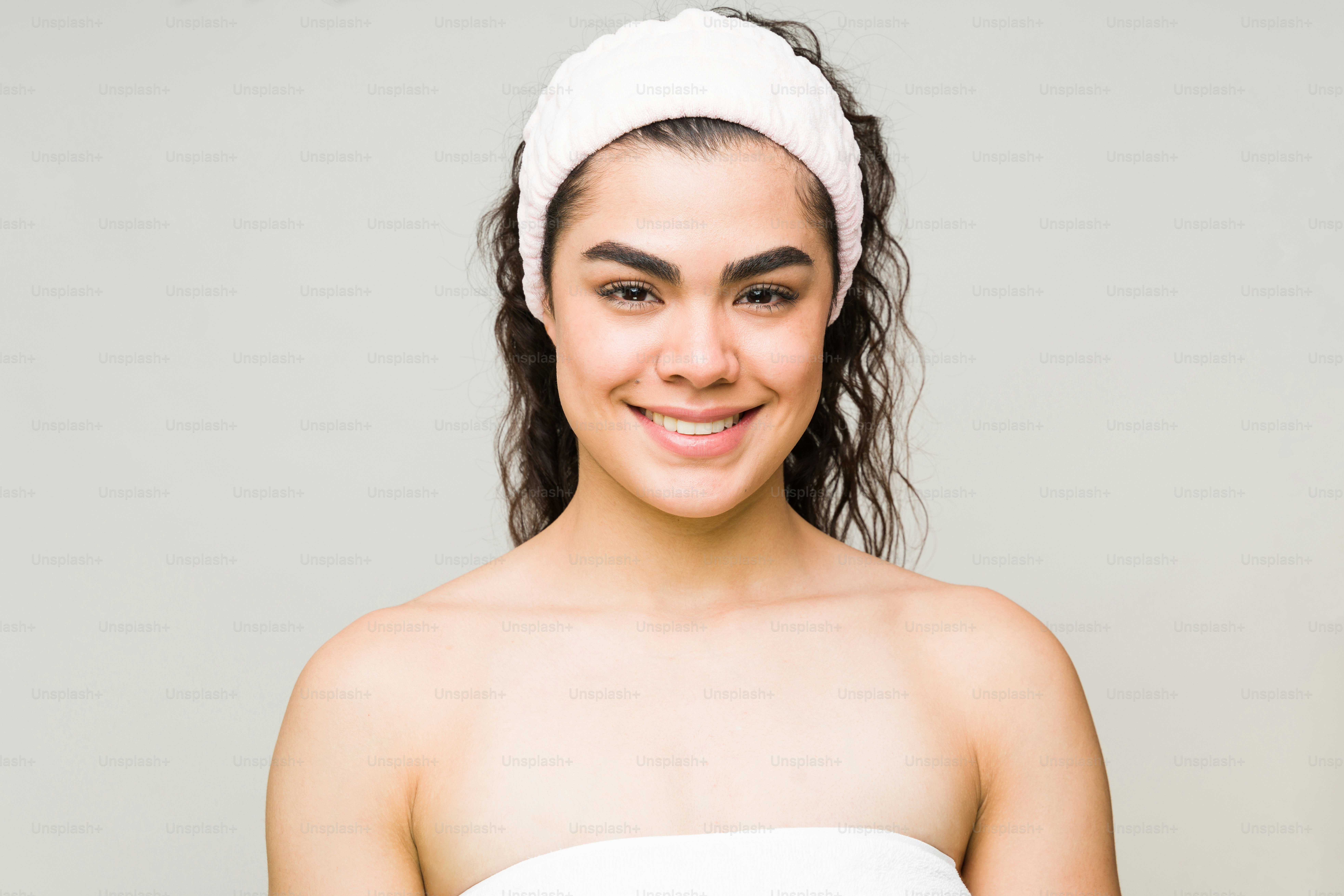 Femme heureuse dans ses années 20 portant une serviette et un bandeau après son bain. Un mannequin beauté sur le point de commencer sa routine de soins de la peau