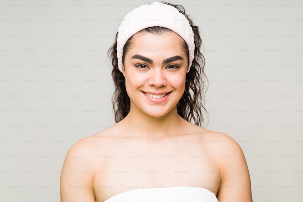 Happy woman in her 20s wearing a towel and a headband after her bath. Beauty model about to start her skin care routine