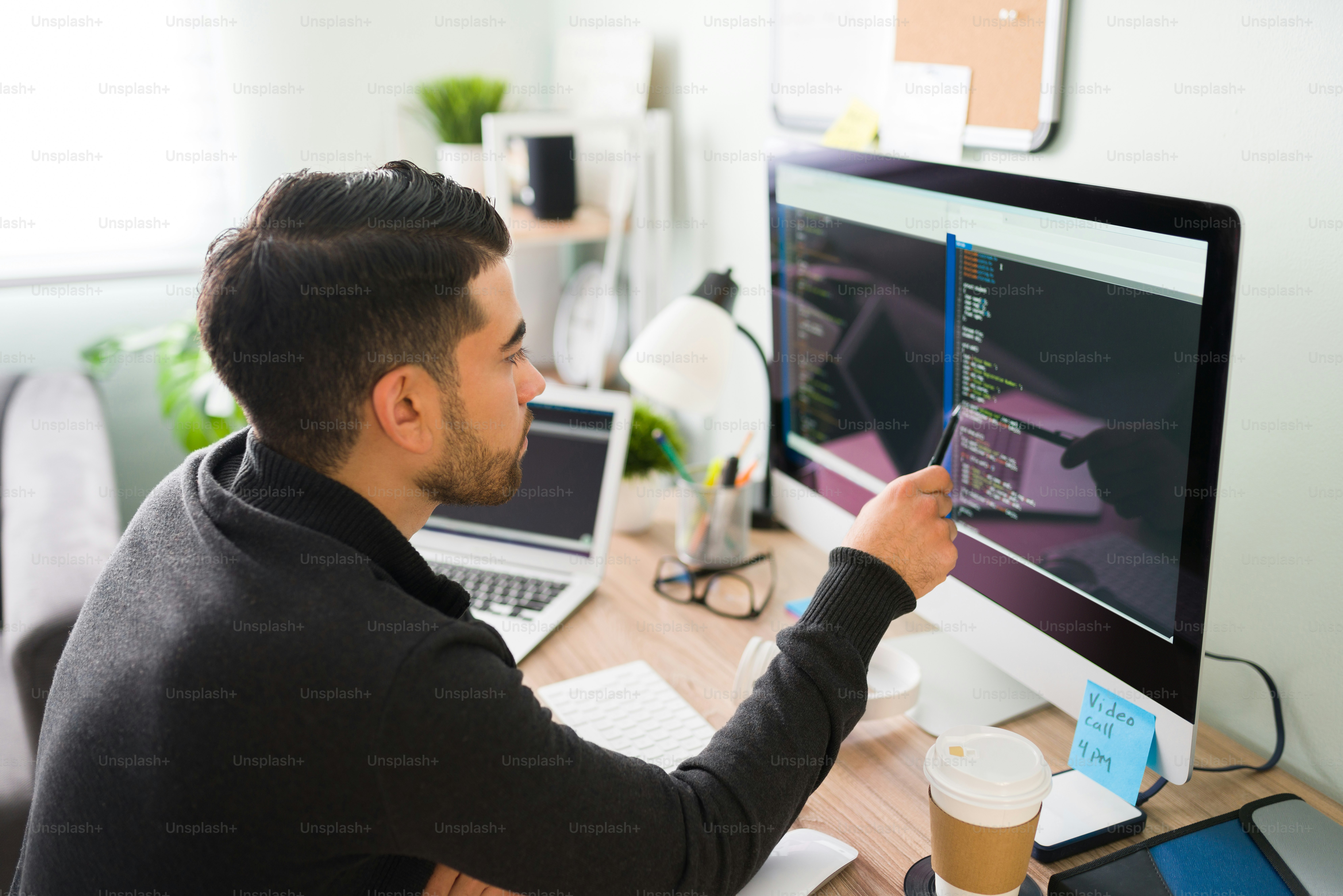 Rear view of a young software developer holding a pen pointing to the computer screen and is analyzing the code