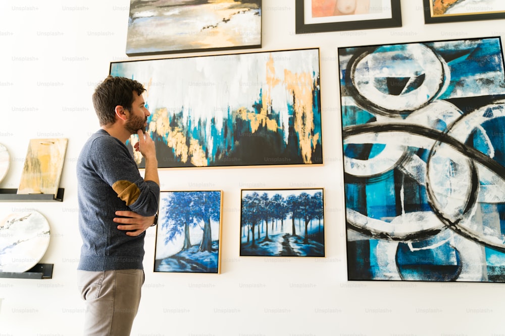 Un bel homme latin de 30 ans est debout et regarde les peintures et les œuvres d’art exposées sur l’exposition de la galerie