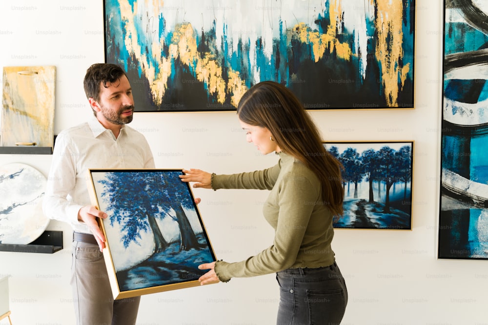 Artista masculino mostrando su pintura a una clienta interesada en comprar algunas obras de arte del exihibiton de la galería de arte