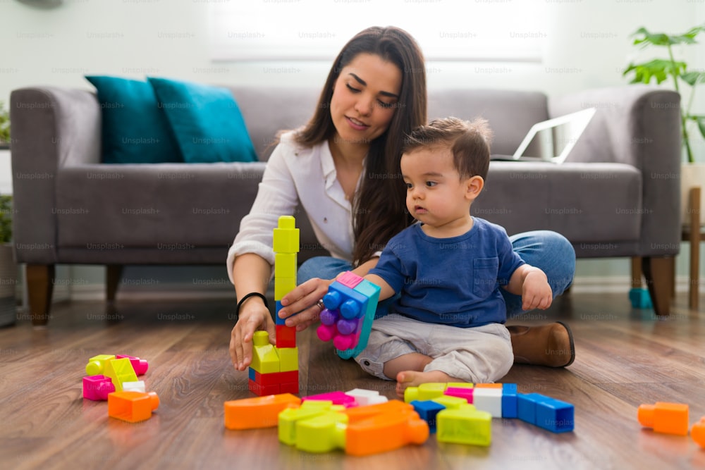 Single mom and baby sitting on living room floor playing with building block toys