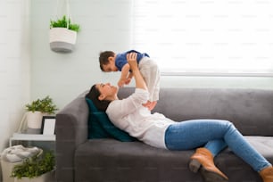 Beautiful young woman relaxing on sofa and holding up her baby boy