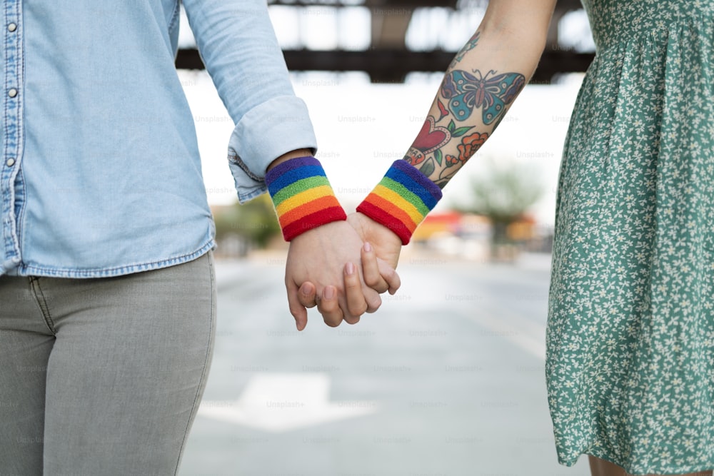 LGBT 권리를 지지하기 위해 손을 잡고 무지개 게이 팔띠를 차고 있는 레즈비언 커플의 클로즈업