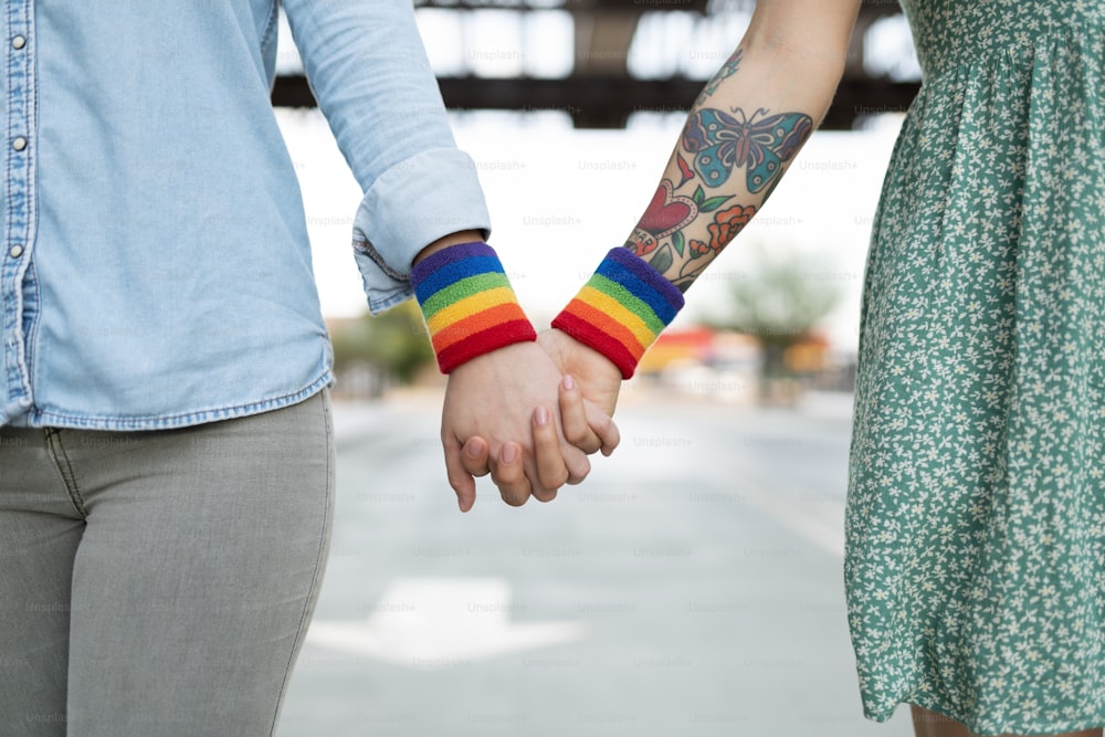 Close up of a lesbian couple holding hands and wearing a rainbow gay arm band in support of LGBT rights
