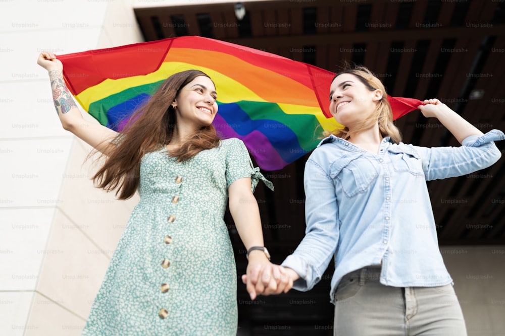 Gay couple looking happy face to face with a fluttering gay pride rainbow flag above their heads