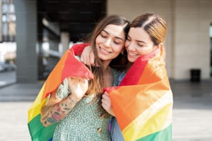 Coppia gay felice che si coccola con una bandiera arcobaleno intorno alle spalle e celebra l'orgoglio gay