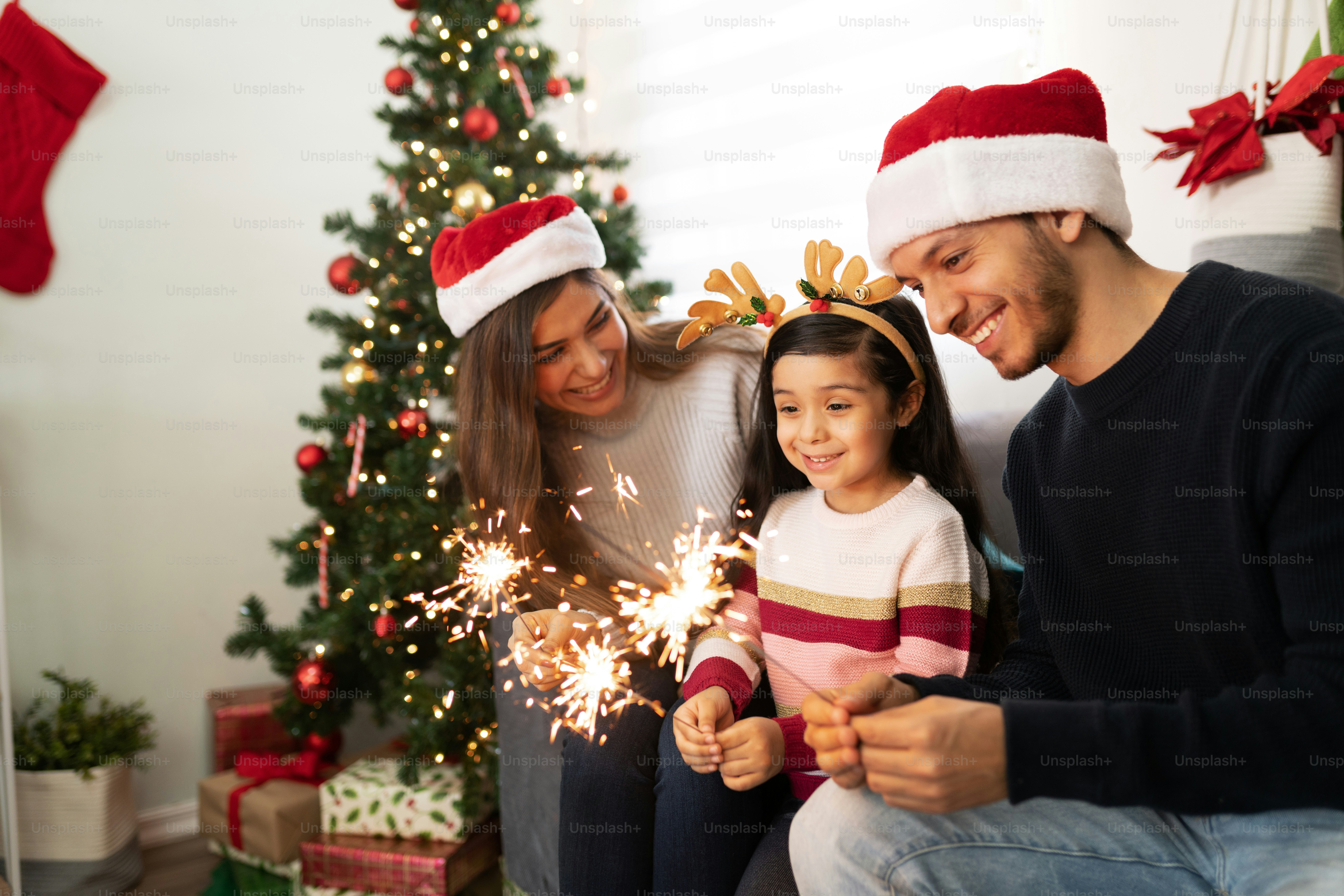 Portrait of a Hispanic family using sparklers at home while a little girl looks very impressed on Christmas