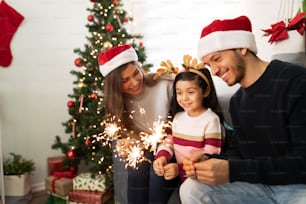 Porträt einer hispanischen Familie, die zu Hause Wunderkerzen verwendet, während ein kleines Mädchen an Weihnachten sehr beeindruckt aussieht