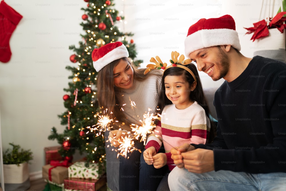 Portrait of a Hispanic family using sparklers at home while a little girl looks very impressed on Christmas